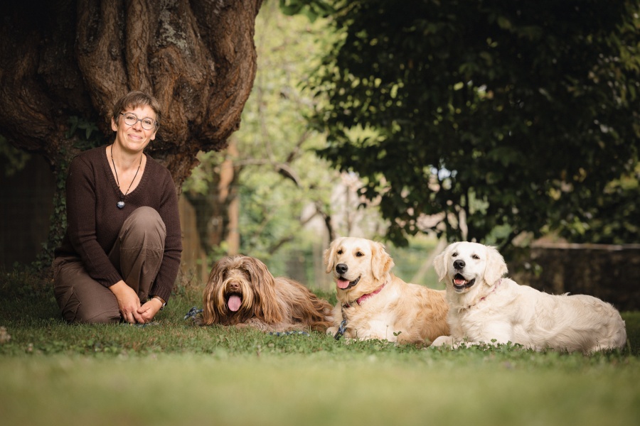 Candice Jouquand pose à genou auprès de ses trois chiennes de race schapendoes et golden retriever, sagement couchées à côté d'elle